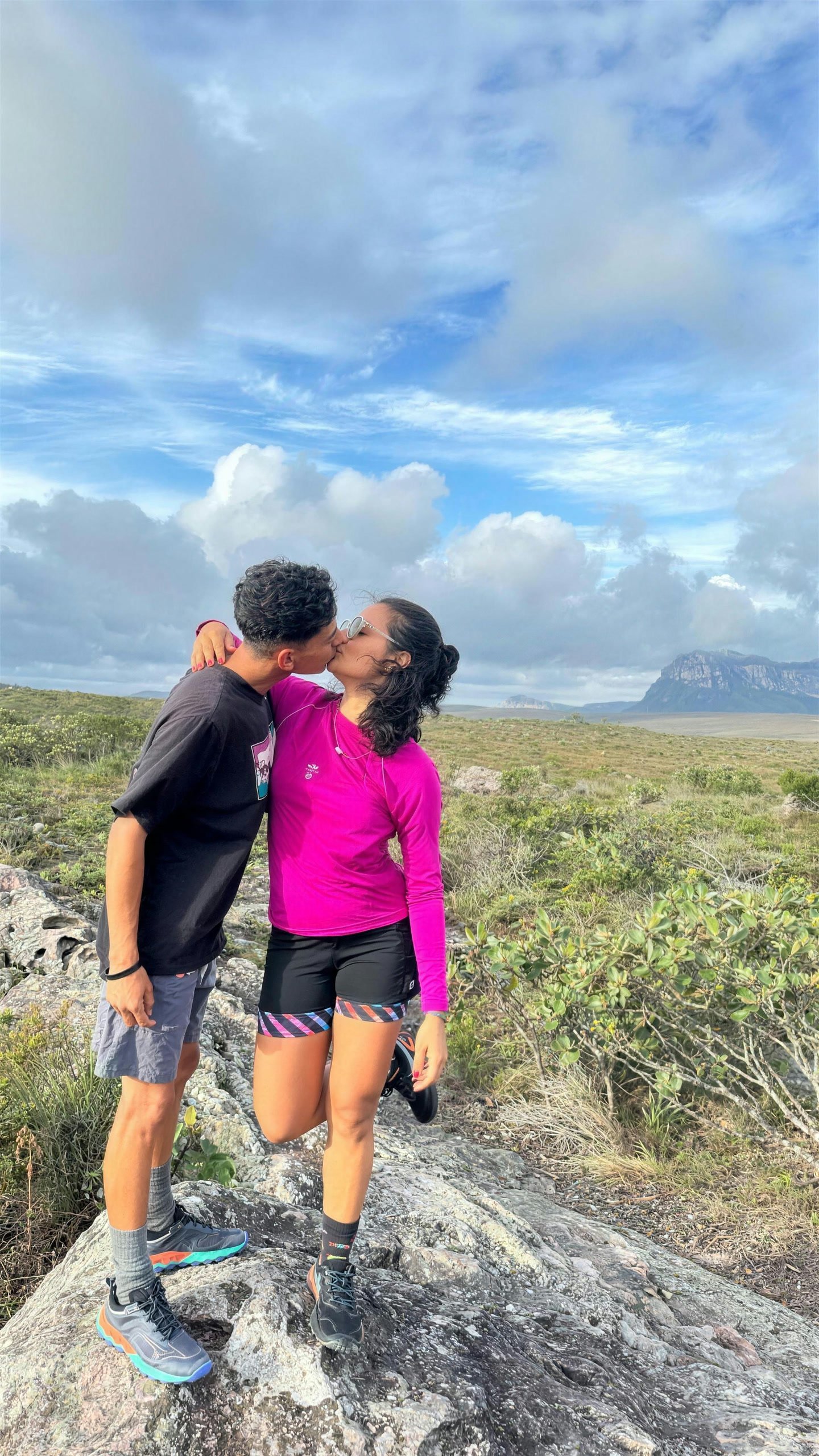Yonara e Pablo se beijando nos gerais da Chapada, com céu azul e o morro ao fundo
