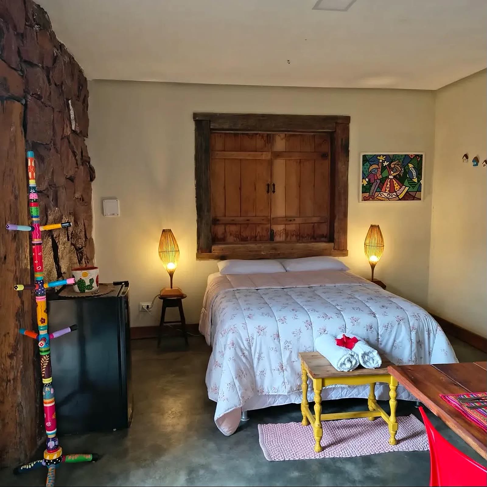 Quarto do chalé com cama de casal, parede de pedra e luminárias acesas