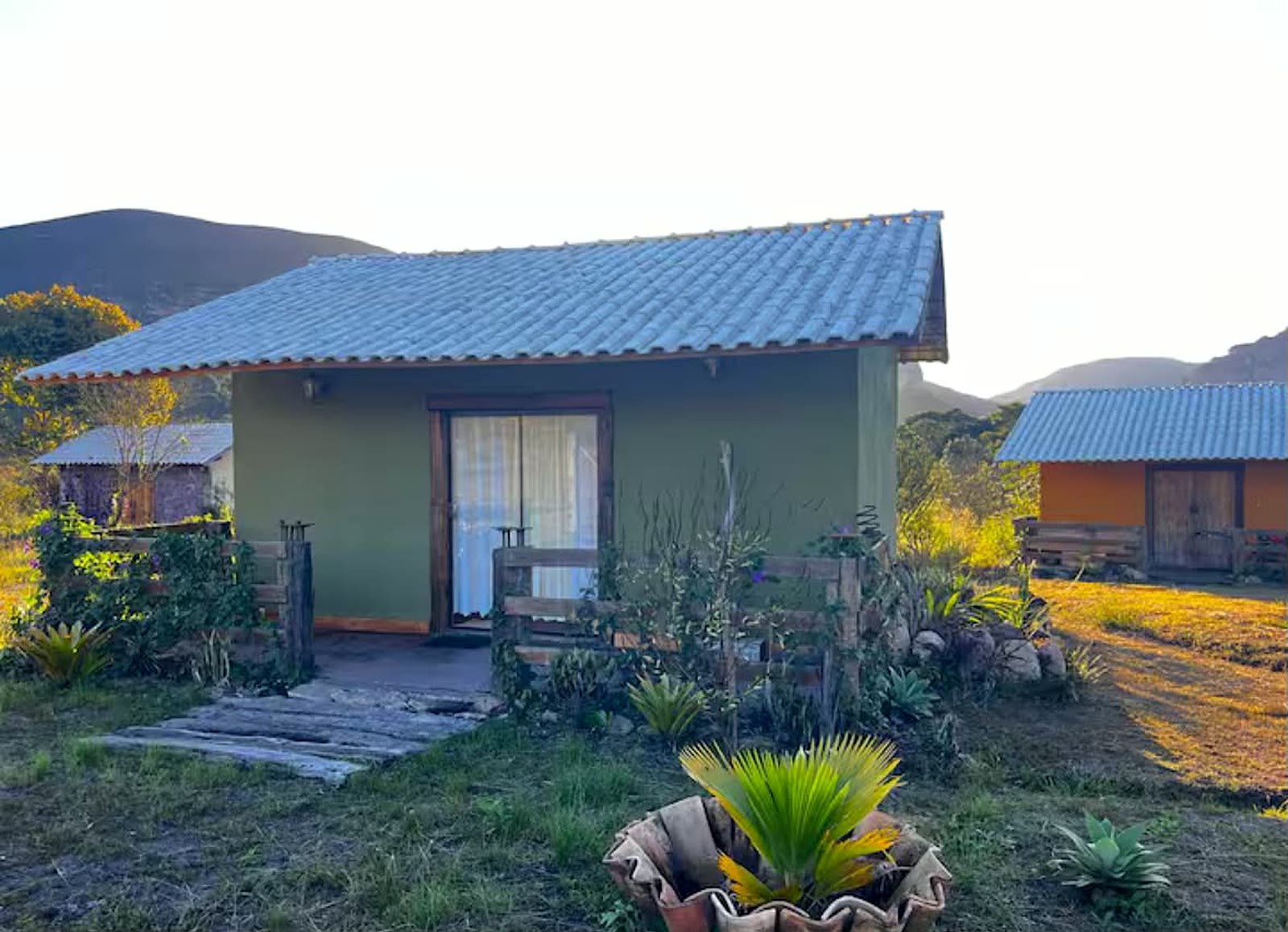 Chalé verde com varanda no pôr do sol, cercado pelos morros da Serra do Sincorá