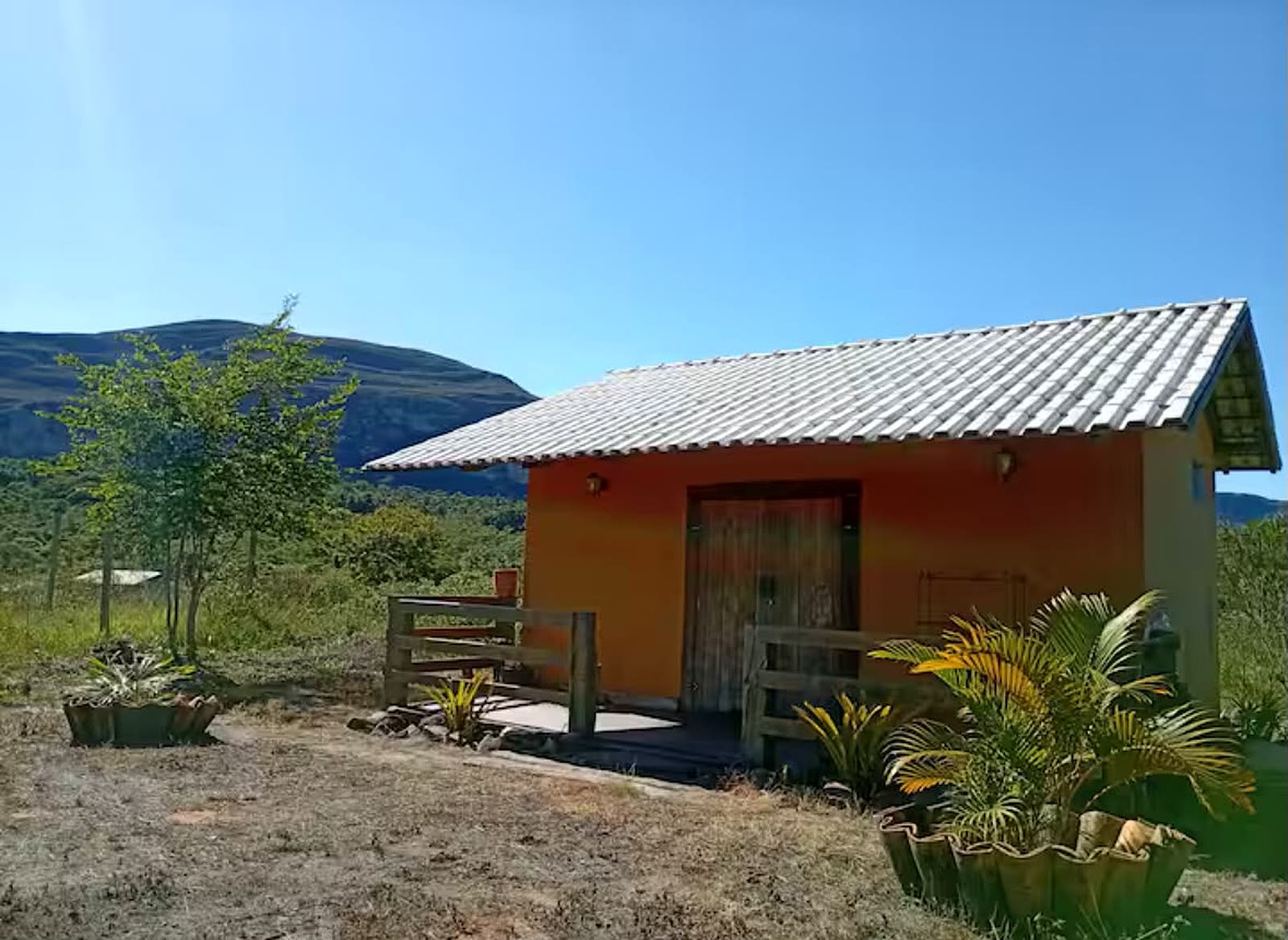 Chalé laranja com varanda sob céu azul, com a Serra do Sincorá ao fundo